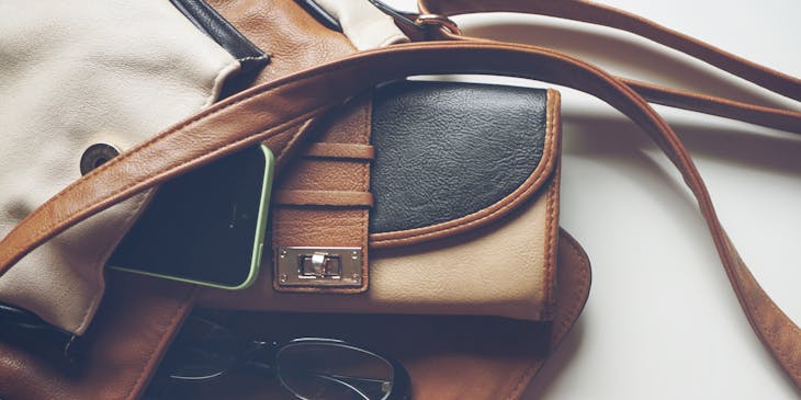 A leather purse filled with pens, a notebook, and a wallet.
