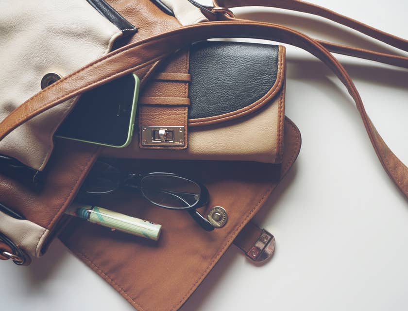 Uma bolsa de couro com canetas, óculos e uma carteira.