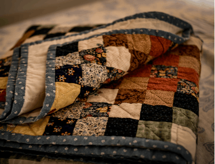 Eine bunte, aufgeschlagene Patchwork-Decke aus einem Quilt-Geschäft liegt auf einem Bett.