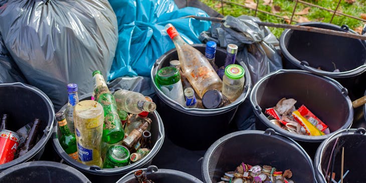 Glass bottles, bottle crowns, and straws separated in black plastic buckets for at a recycling center.