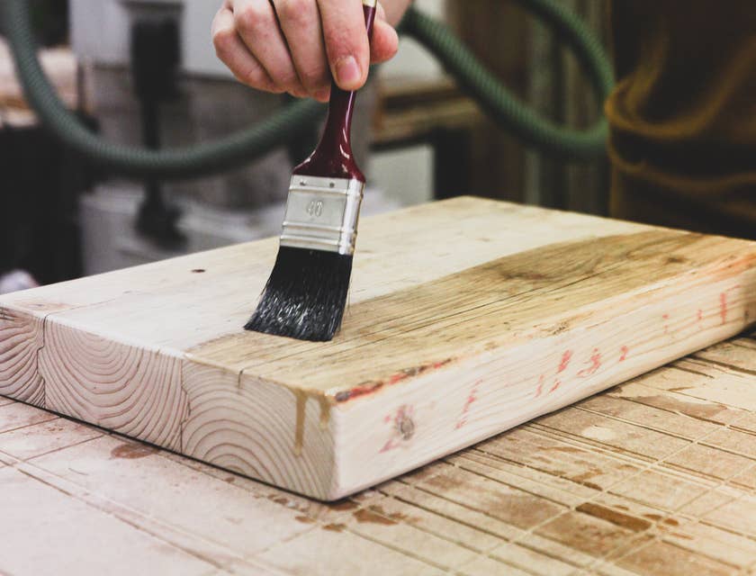 Pessoa fazendo um acabamento de pintura em uma placa de madeira.
