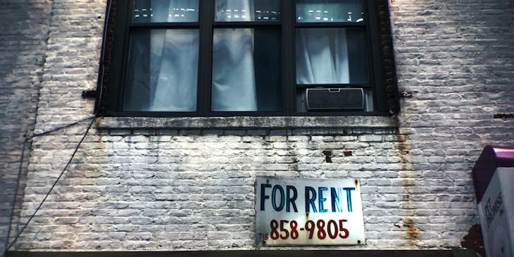 Rental sign outside on a brick wall under a window.