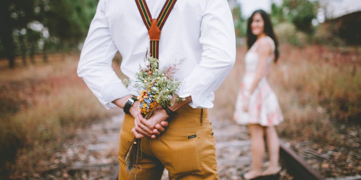 A man holding flowers behind his back to give in a romantic gesture.