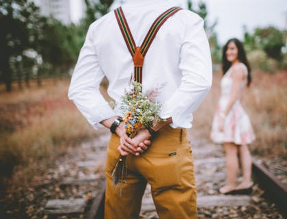 Un hombre sosteniendo un ramo de flores detrás de su espalda para dárselas a su novia en un negocio romántico.