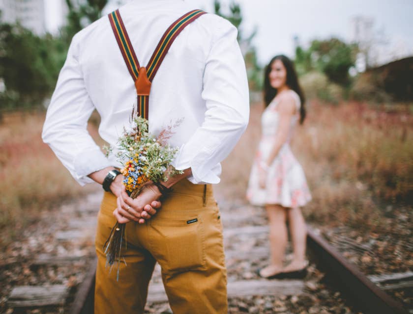 Un homme tenant des fleurs derrière son dos pour les offrir dans un geste romantique.