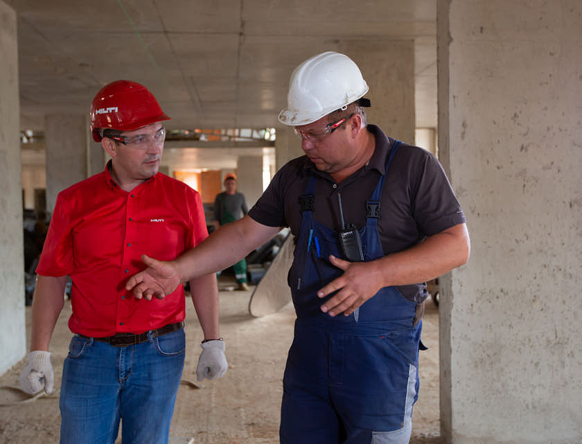 Dois homens usando óculos de segurança e capacete em um canteiro de obras.