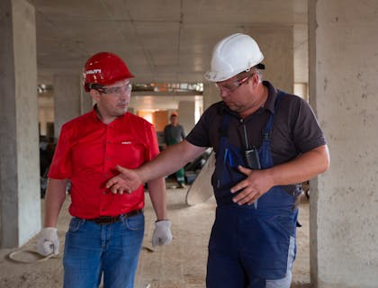 Two men wearing safety glasses and hard hats on construction site.