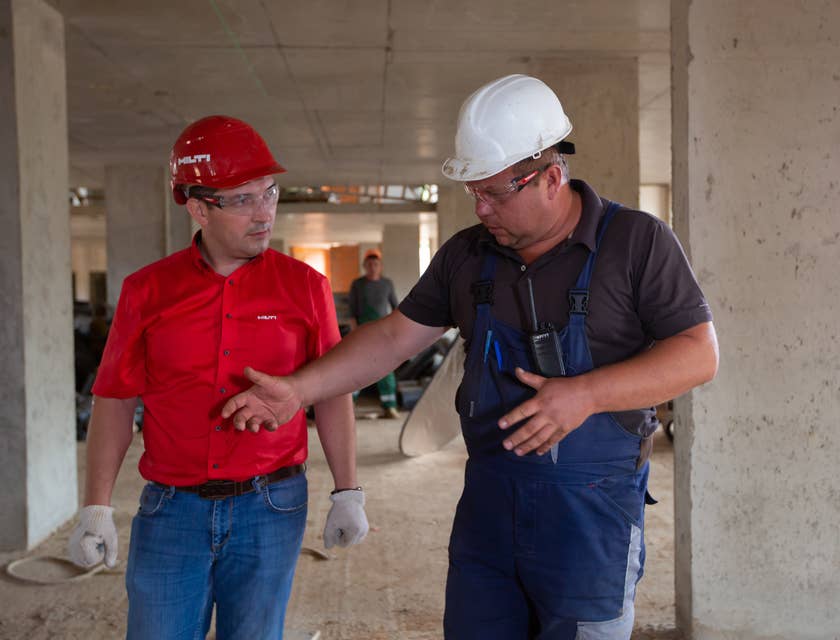 Deux hommes portant des lunettes de sécurité et des casques sur un chantier de construction.