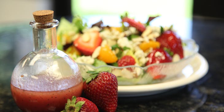 Strawberry salad dressing in a glass bottle beside a salad