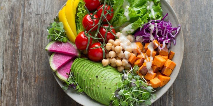 Salad comprising leafy greens, chickpeas, sliced avocado, cocktail tomatoes on the vine, and more.
