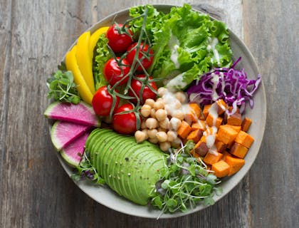 Un'insalata con verdure a foglia verde, ceci, avocado a fette, pomodorini, cavolo, anguria e altro ancora.