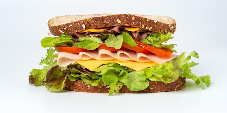Whole-wheat sandwich crammed with cheese, lunch meats, sliced tomato, and leafy greens.
