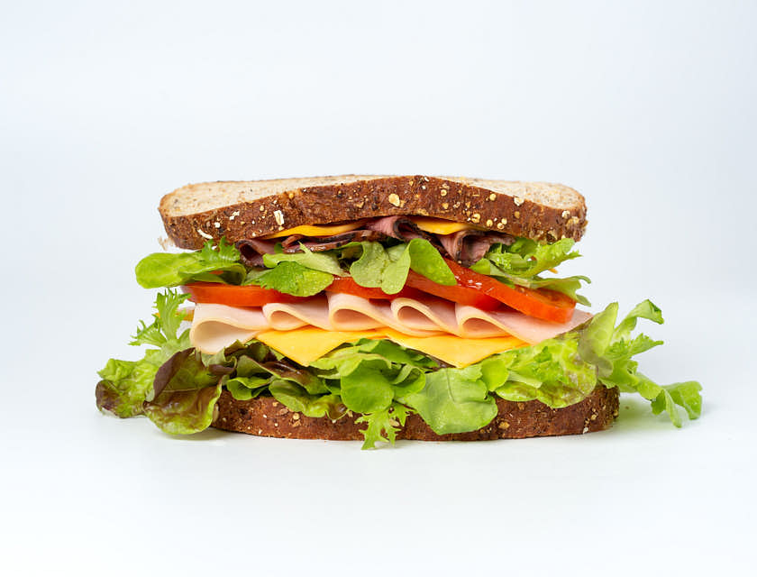 Un sándwich con rebanadas de jamón de pavo, tomate, quedo amarillo y lechuga en pan integral en un restaurante de sándwiches.