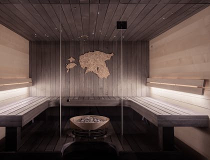 Un sauna lambrissé avec bancs autour d'un poêle de sauna et décoration en liège au mur.