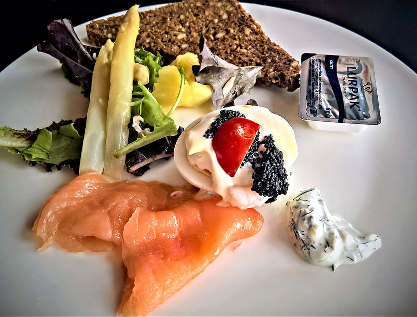 Un plat scandinave au saumon et pain de seigle sur une plaque en céramique blanche.
