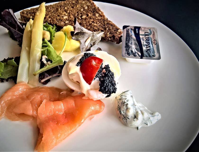 Un plat scandinave au saumon et pain de seigle sur une plaque en céramique blanche.