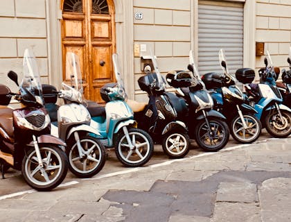 Fila de scooters azules, blancos y negros fuera de un negocio de tours en scooter.