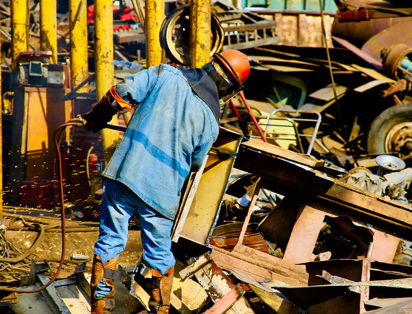 Ein Schrotthändler in blauer Arbeitskleidung und mit Helm bereitet das Recyceln von Altmetall auf einem Schrottplatz vor.