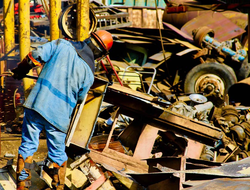 Ein Schrotthändler in blauer Arbeitskleidung und mit Helm bereitet das Recyceln von Altmetall auf einem Schrottplatz vor.