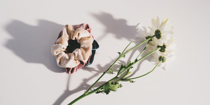 Scrunchies on a white surface with flowers next to them.
