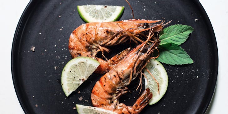 Dos camarones adornados con rodajas de limón y dos hojas de albahaca.