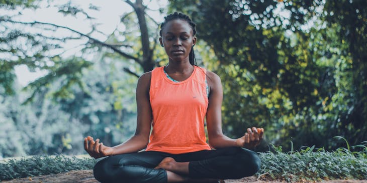 A woman practicing self-care by meditating outdoors.