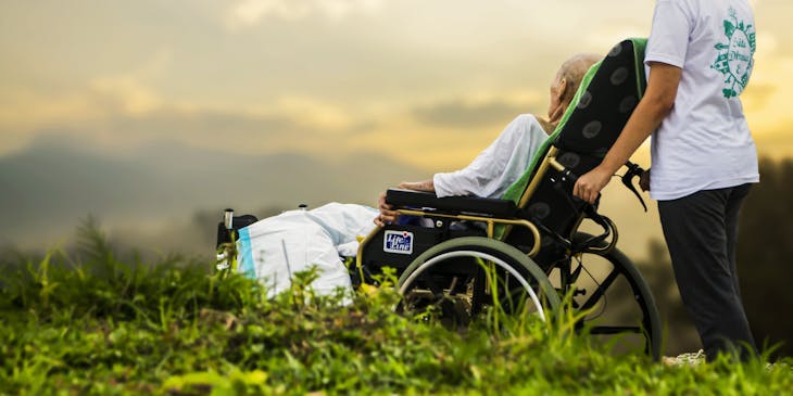 A woman pushing a senior lady's wheelchair outside.