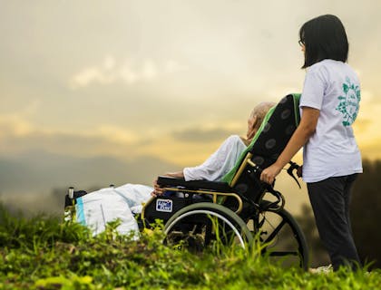 Mulher empurrando a cadeira de rodas de uma senhora idosa.