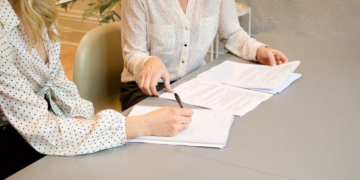 Deux femmes en chemise blanche à pois travaillant sur des documents.
