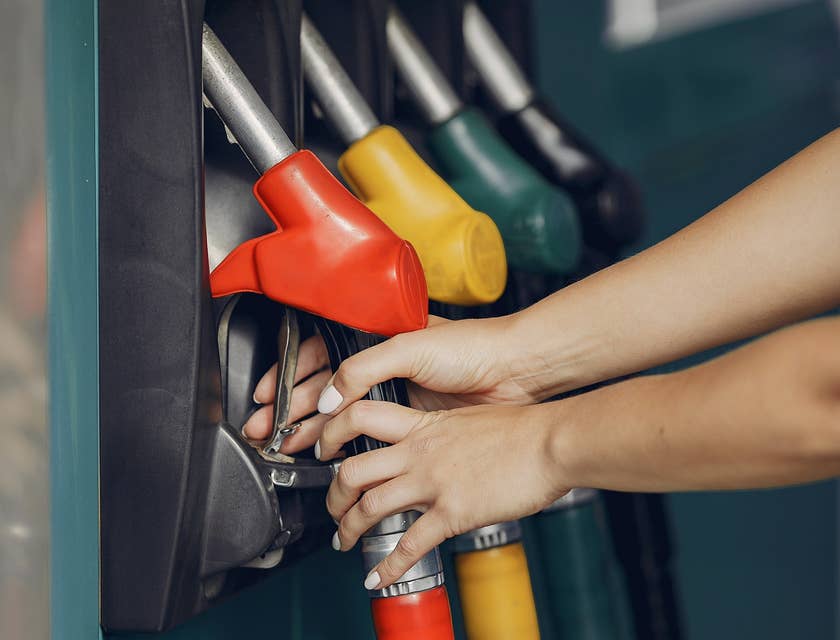 Woman's hands picking up a red gas pistol pump at a service station.