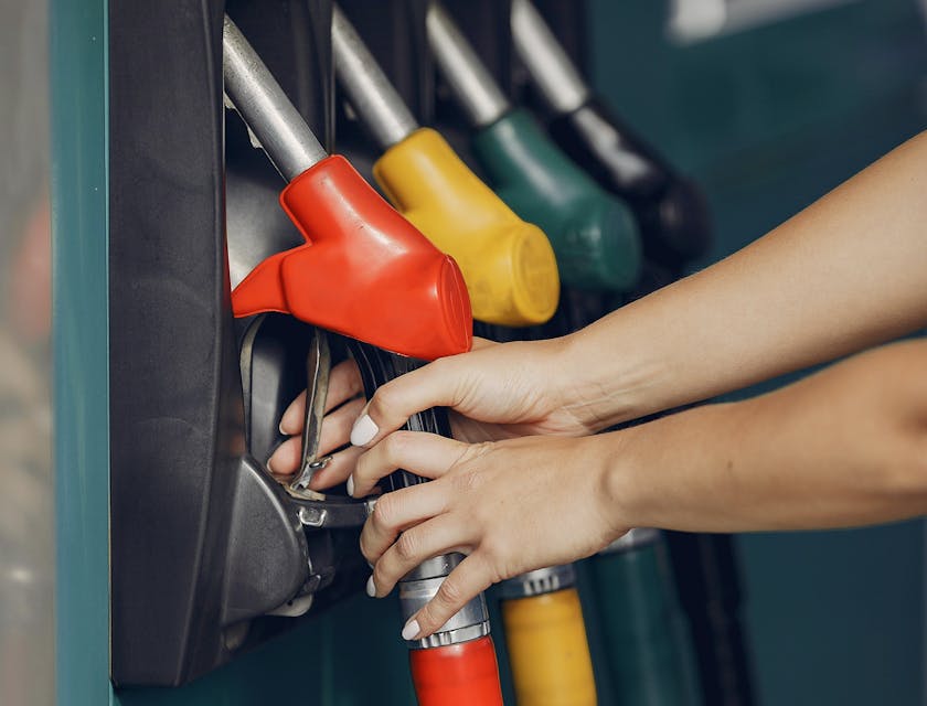 Woman's hands picking up a red gas pistol pump at a service station.