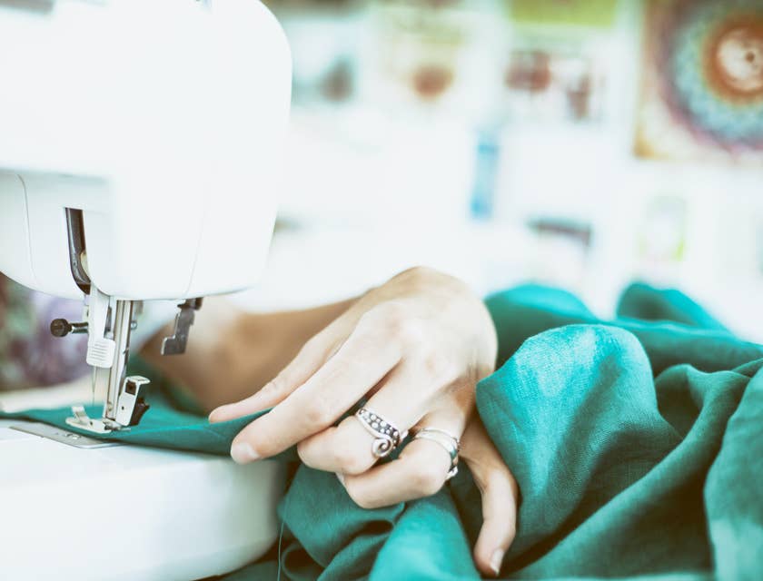 Une personne qui coud une blouse verte à la machine à coudre dans un atelier de couture.