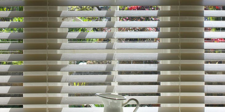 A white pitcher in front of blinds.