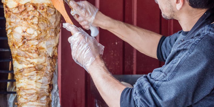 A man cutting off pieces of meat from a shawarma.