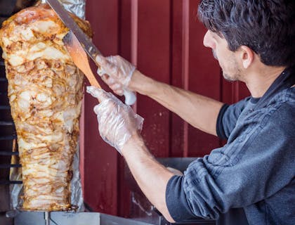 Hombre cortando trozos de carne de un shawarma en un restaurante shawarma.
