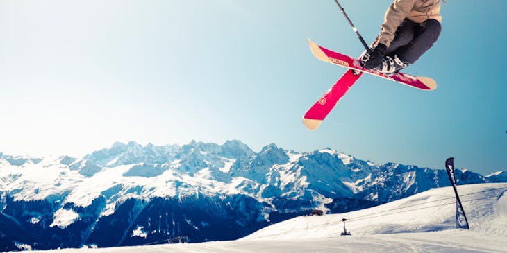 A man in a brown jacket doing a trick while skiing.