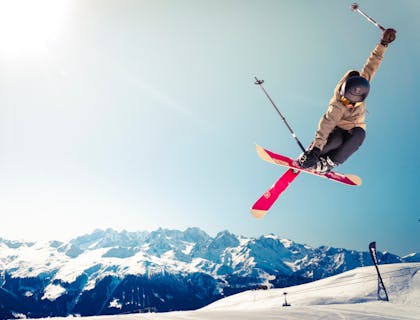Un homme en veste marron faisant un trick en ski.