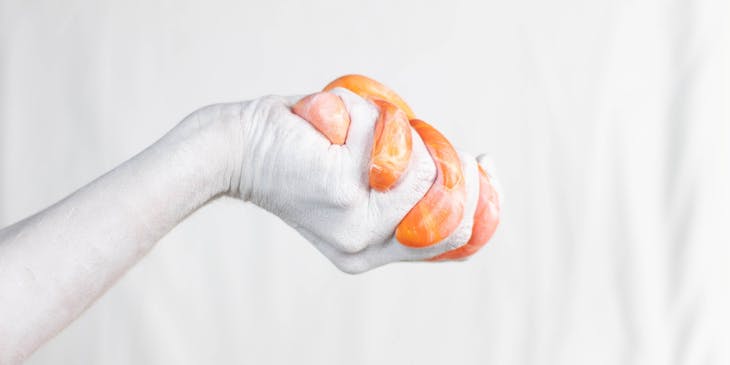 A left hand squeezing an orange-colored slime.