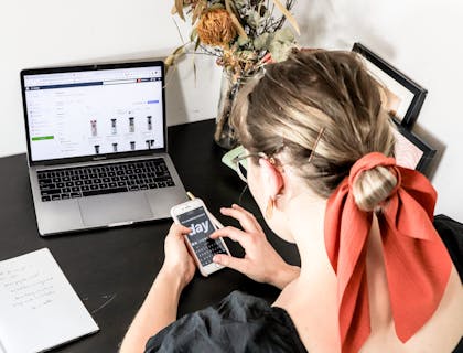 A person with a phone in hand sitting in front of laptop.