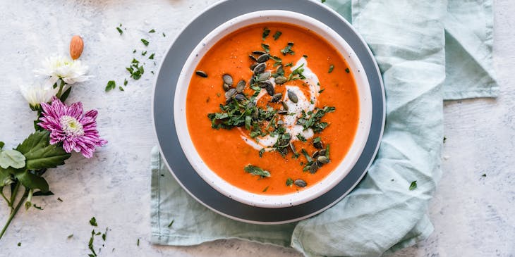 Un bol blanc de soupe à la tomate à côté d'une cuillère à manche bleu et un petit bol de tomates grappes.