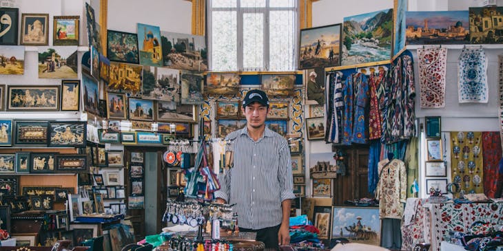 Man with cap surrounded by trinkets in souvenir shop.