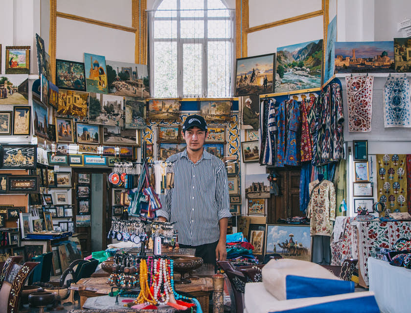 Man with cap surrounded by trinkets in souvenir shop.