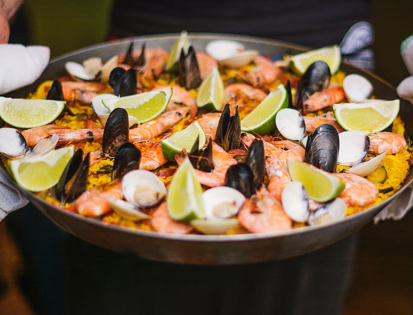 Eine herzhafte Paella, garniert mit Limetten-Scheiben, wird in einer Pfanne in einem authentischen spanischen Restaurant serviert.
