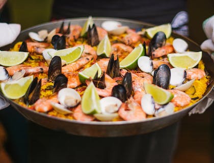 Paella servita nella paellera, decorata con delle fette di limone sopra il tavolo di un ristorante spagnolo.