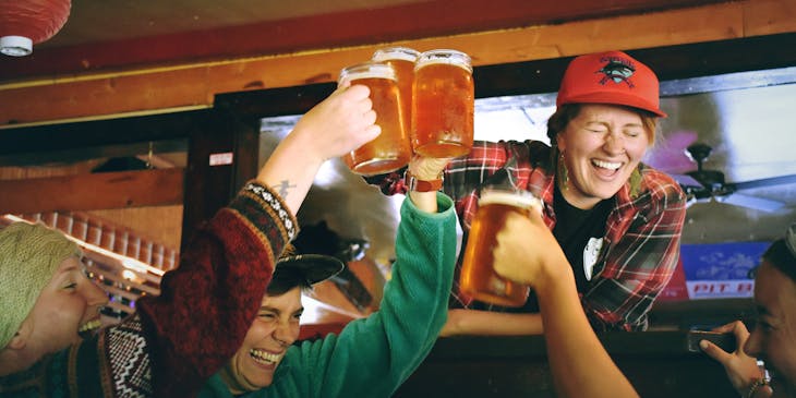 People in sports bar tapping beer mugs together.