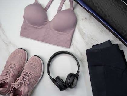 Produtos de uma loja de roupas esportivas e um par de headphones em cima de um tapete de ginástica.