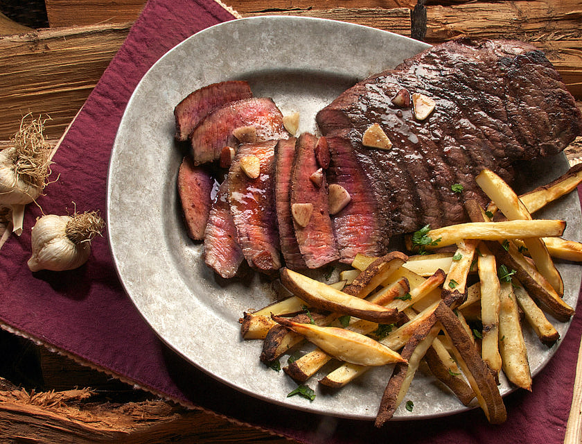 Un filete con papas a la francesa sobre un plato blanco en un restaurante de carnes.