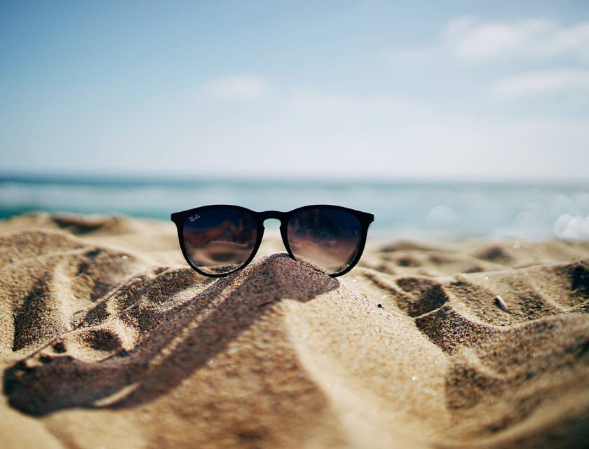 Eine Sonnenbrille liegt auf einem Sandstrand mit dem Meer im Hintergrund.