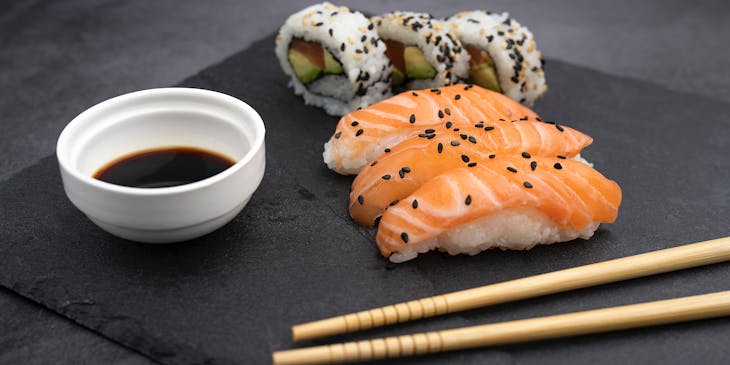 Nigiri and California rolls with chopsticks on black plate.