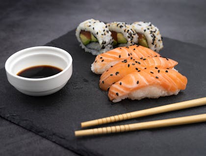 Nigiri and California rolls with chopsticks on black plate.
